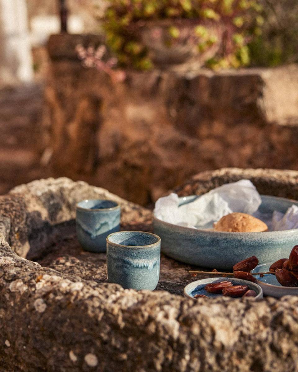 Blau-türkises Keramikgeschirr mit Datteln auf rustikalem Stein im Garten
