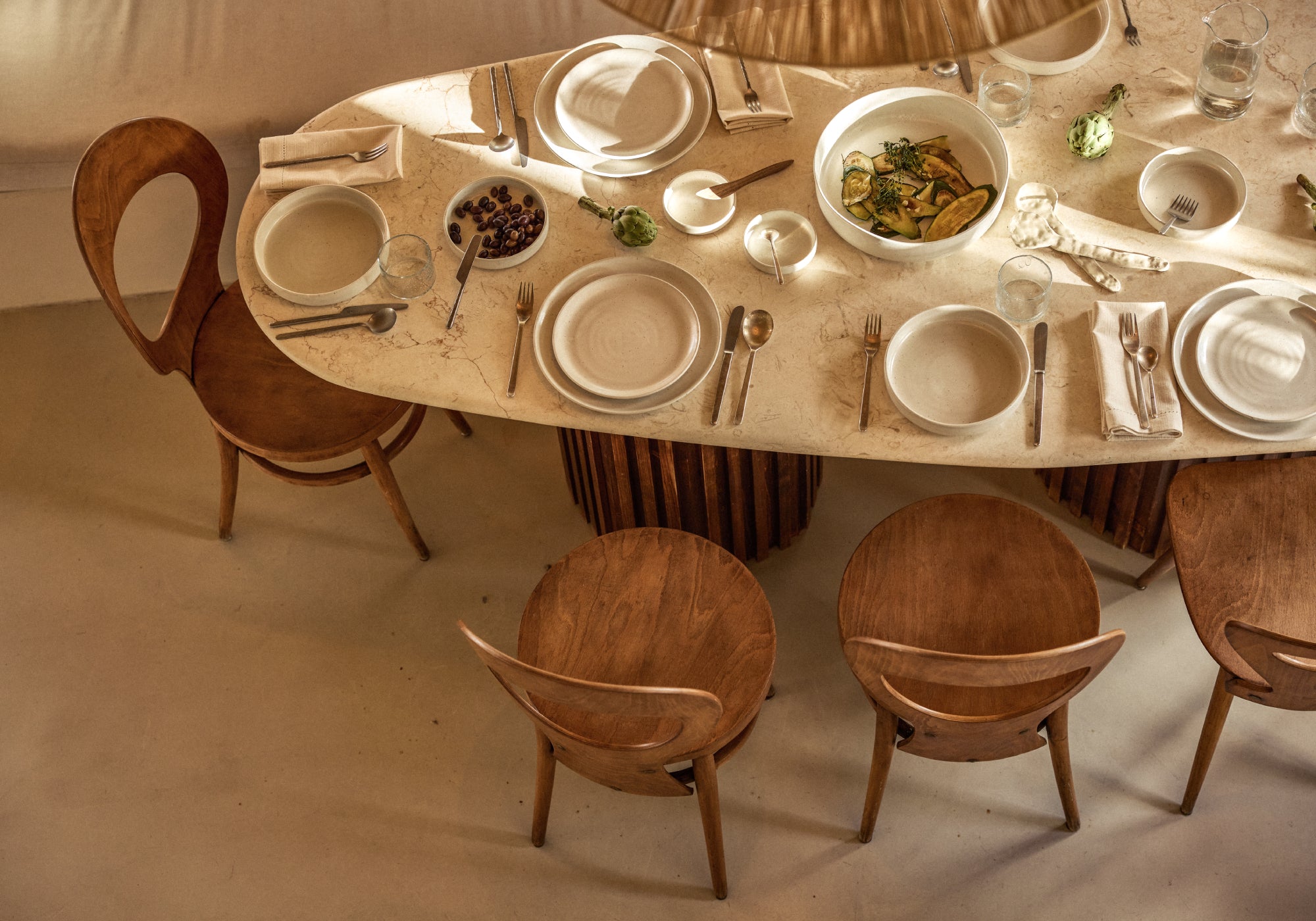 Gedeckter Esstisch mit beigen Tellern und Designer-Holzstühlen von oben fotografiert