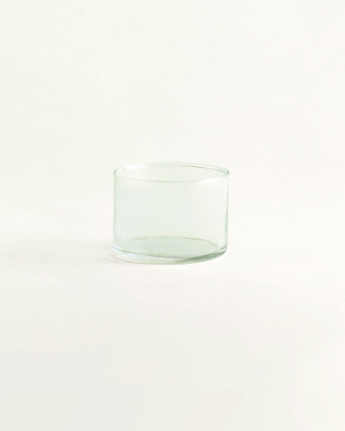 Einzelnes niedriges Trinkglas aus grünlichem Glas, breite Form, vor hellem Hintergrund.